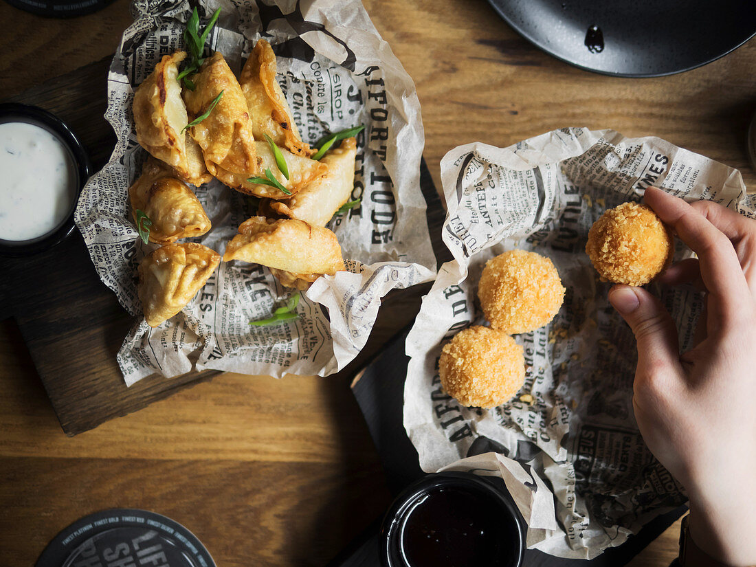 Hand holding deep fried cheese balls near plate with dumplings garnished with green herbs
