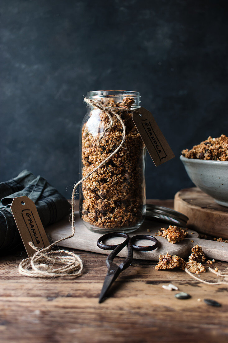 Glass jar of fresh millet and quinoa granola with label placed on wooden table
