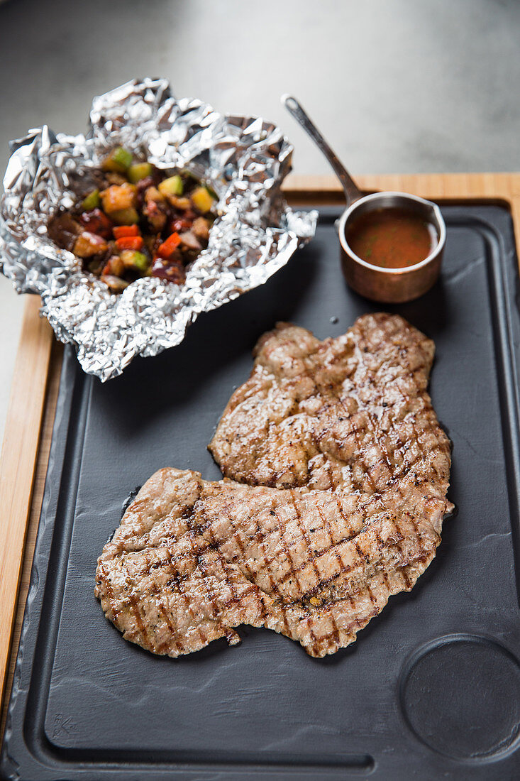 Piece of tasty grilled meat placed on tray near sauce on table