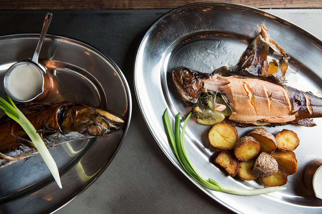 Yummy roasted fish and potatoes served with ripe scallion and cream sauce on metal plate