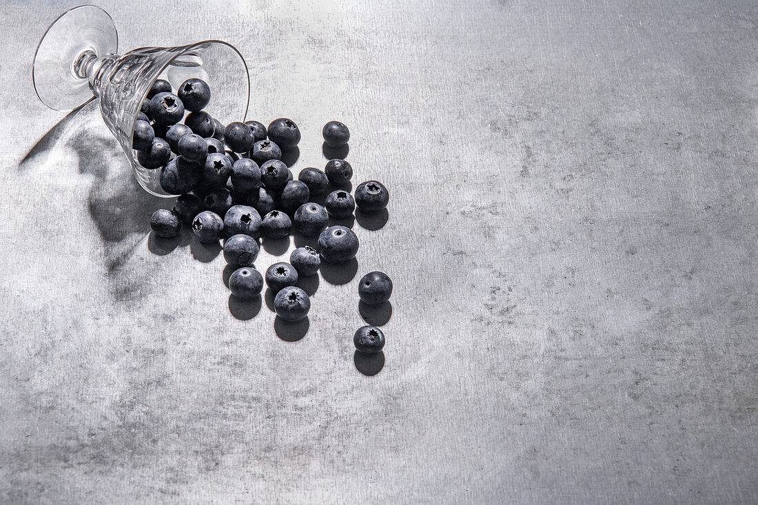 Blaubeeren neben umgekipptem Glas