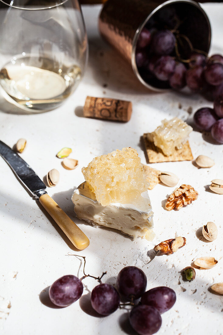 A cheeseboard with brie topped with honeycomb, crackers, walnuts, pistachios, grapes and white wine