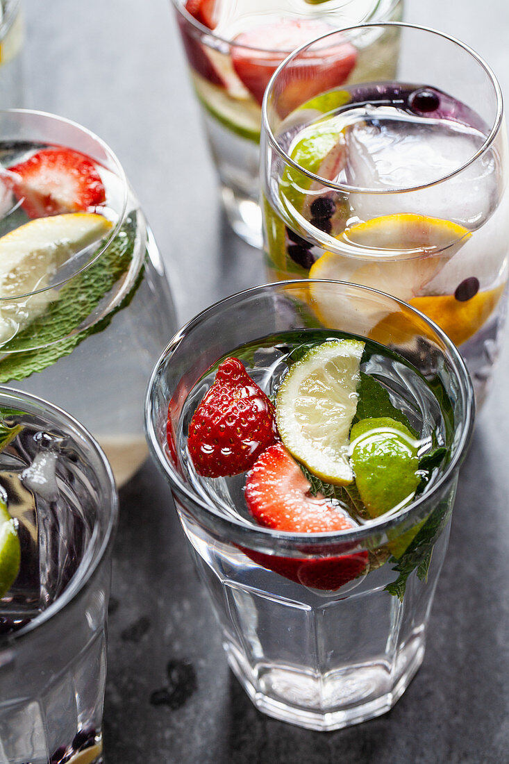 Various glasses of water filled with fruit, mint and ginger