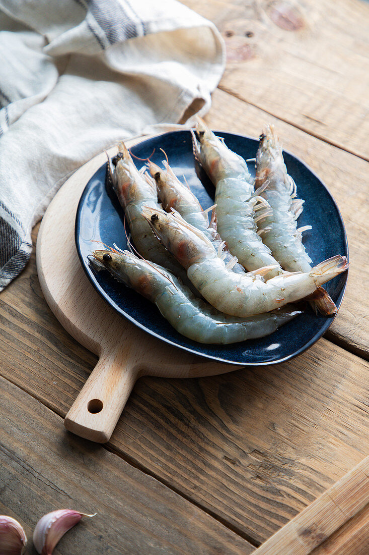 Raw gray shrimps on big blue plate on cutting board on rustic wooden table