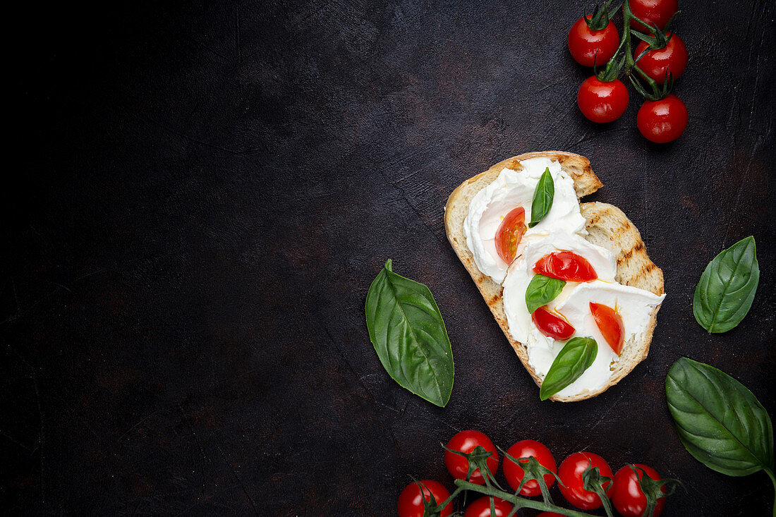 Crunchy toast smeared with cream cheese and decorated with basil leaves and pieces of cherry tomatoes