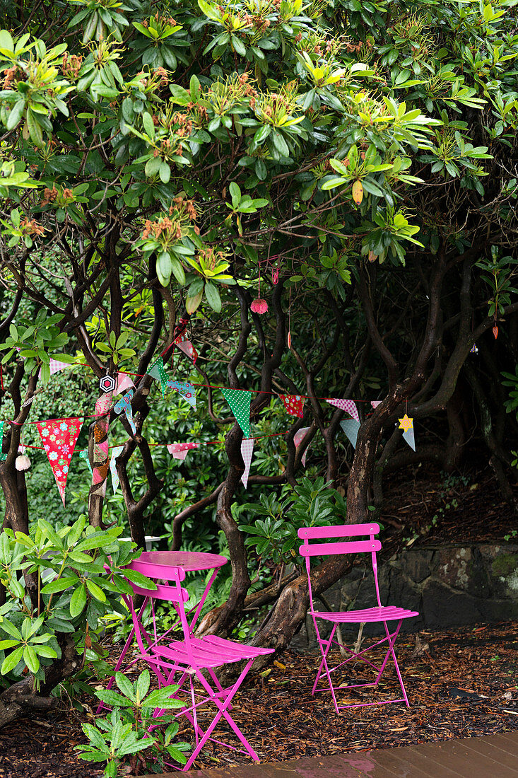 Pinke Gartenmöbel unterm Baum mit Wimpelketten im Garten
