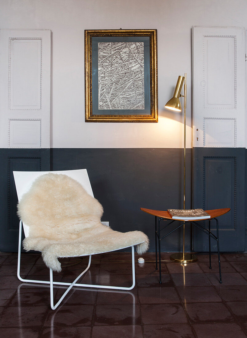 Sheepskin rug on easy chair, side table and standard lamp below drawing on wall