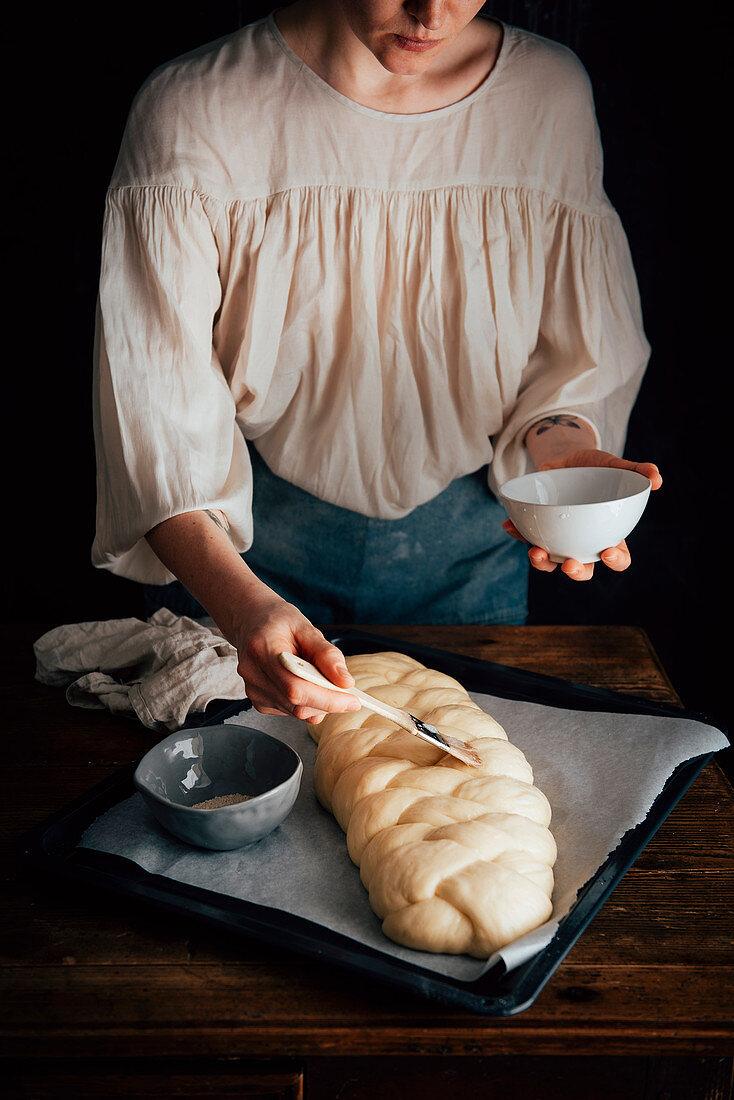 Frau beim Einpinseln eines ungebackenen Challah-Brotzopfs