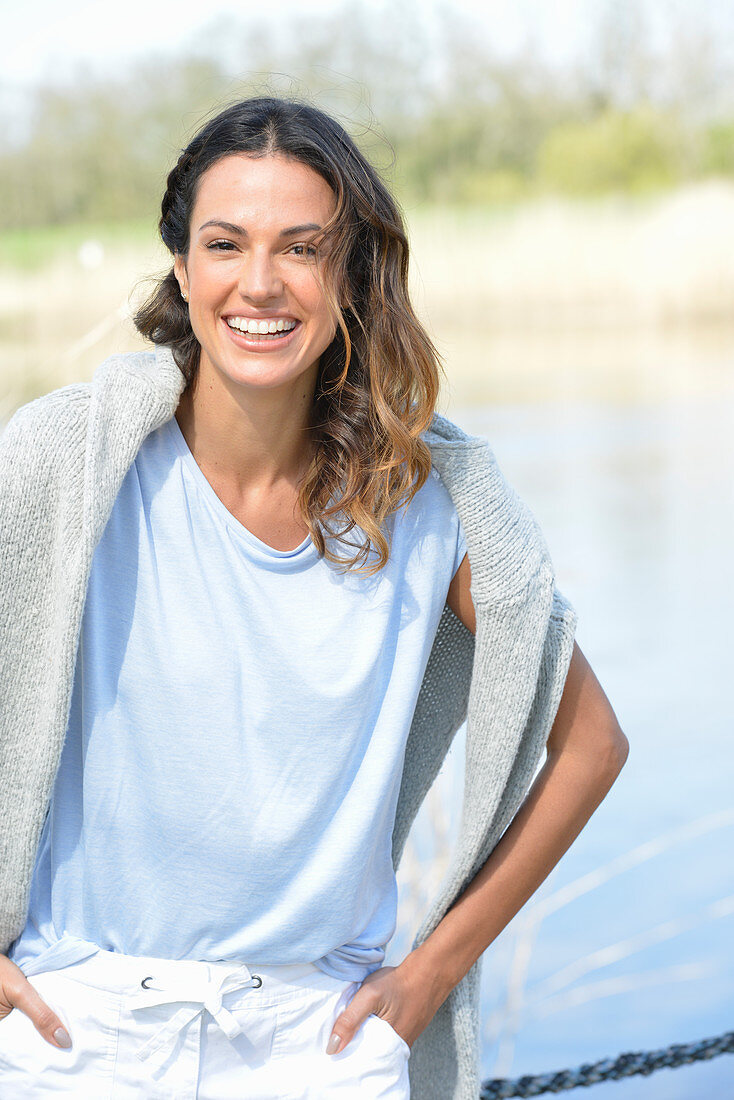 Junge Frau in hellblauem T-Shirt, Pulli über den Schultern und weißen Shorts am Fluss