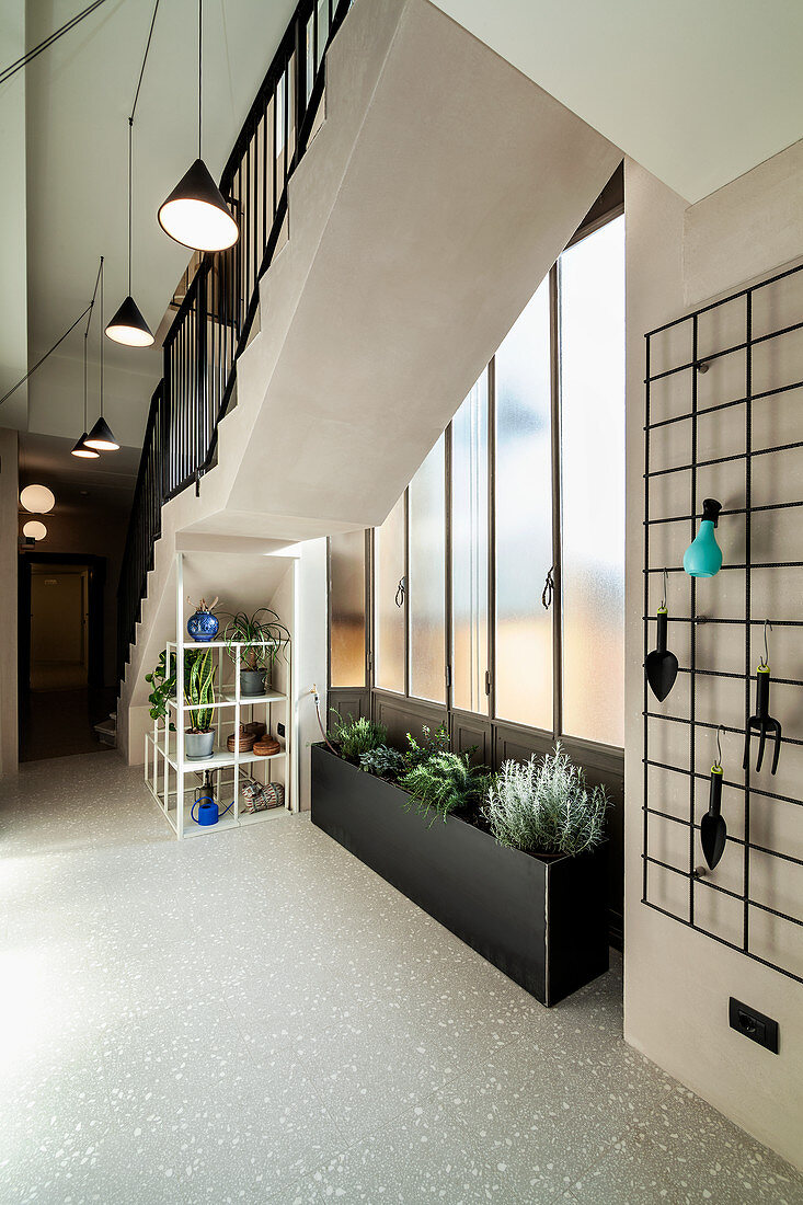 Stair well decorated with planting trough, plants on shelves and gardening utensils hung from metal grille on wall