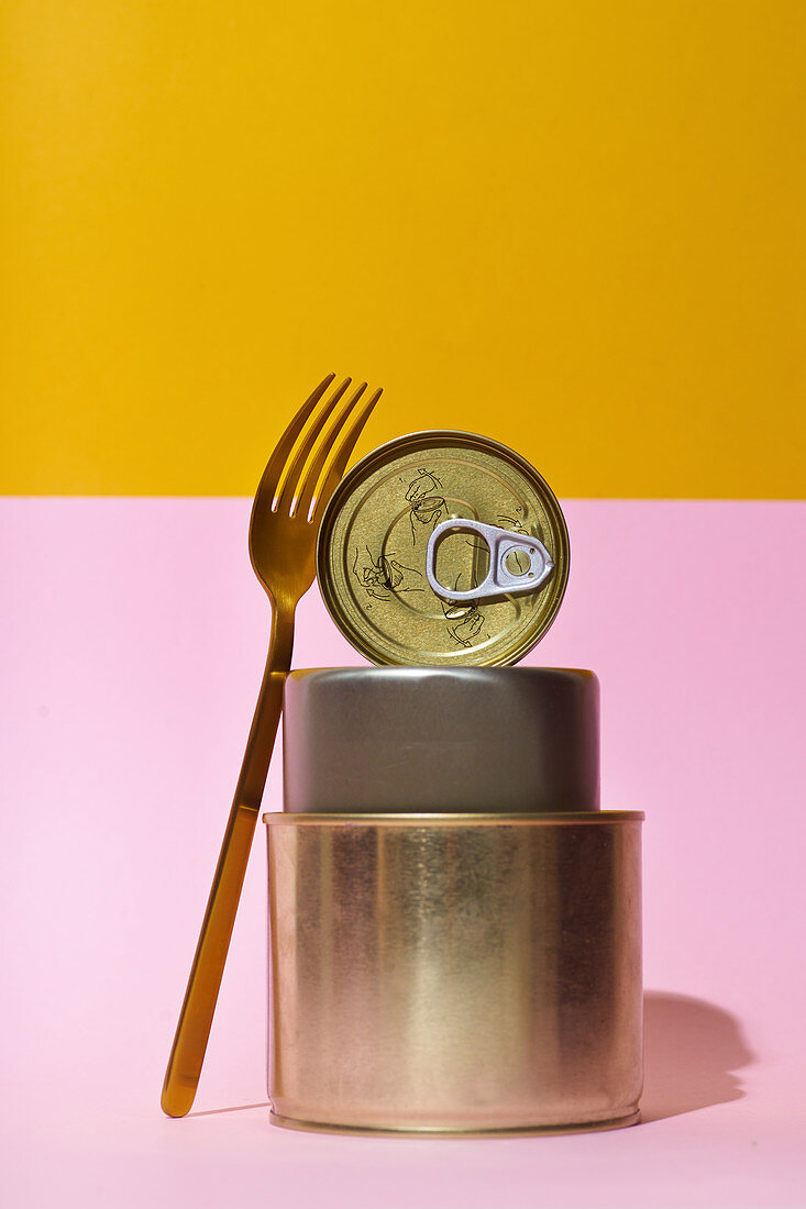 Three tins and a fork against a pink and yellow background
