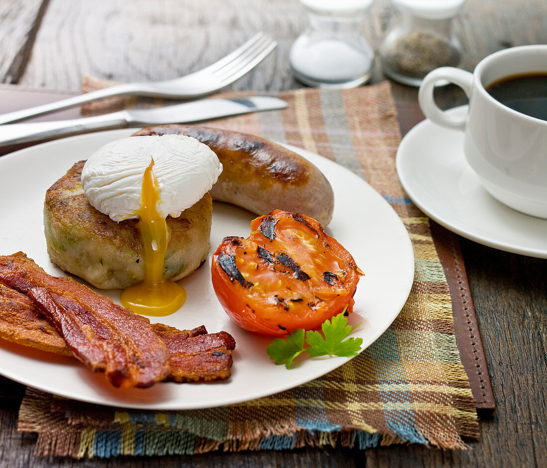 Englisches Frühstück mit knusprigem Speck, pochiertem Ei, Grilltomate, Wurst und Hash Browns