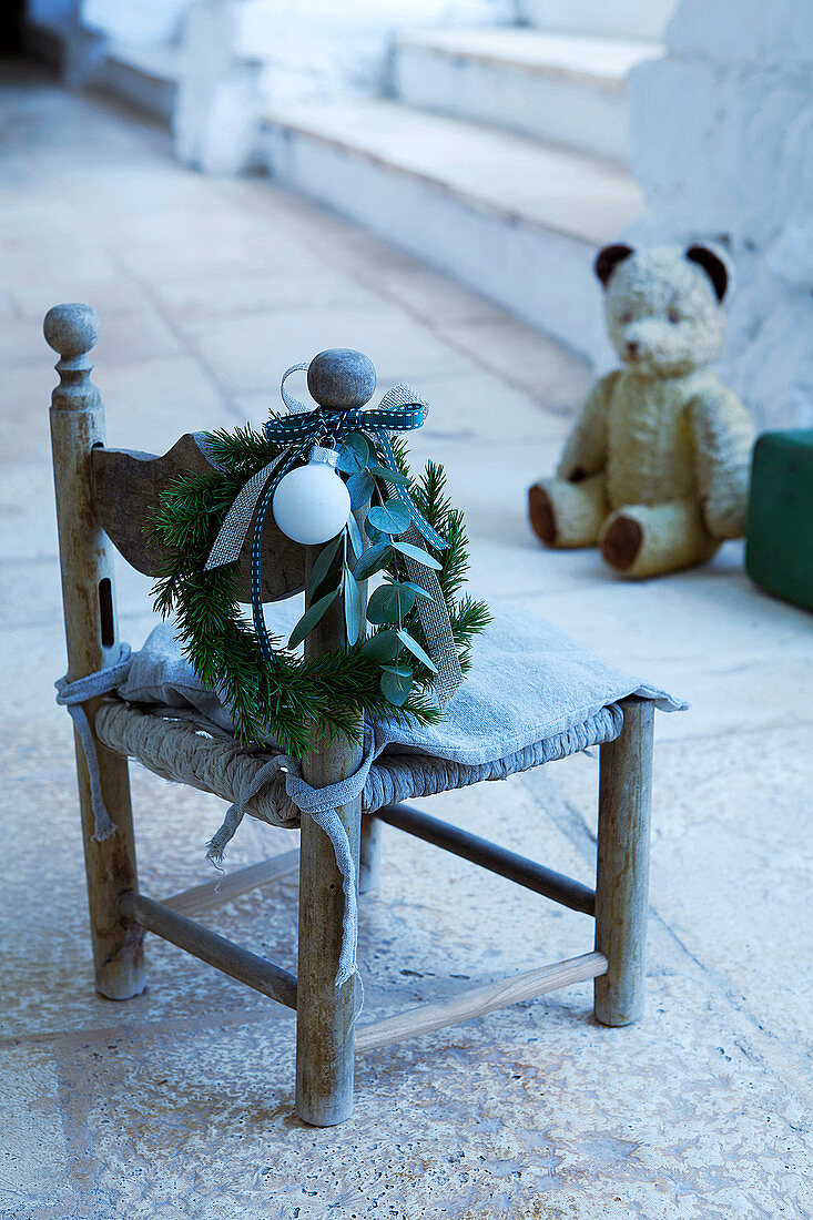 Christmas wreath on child's chair with teddy bear in background