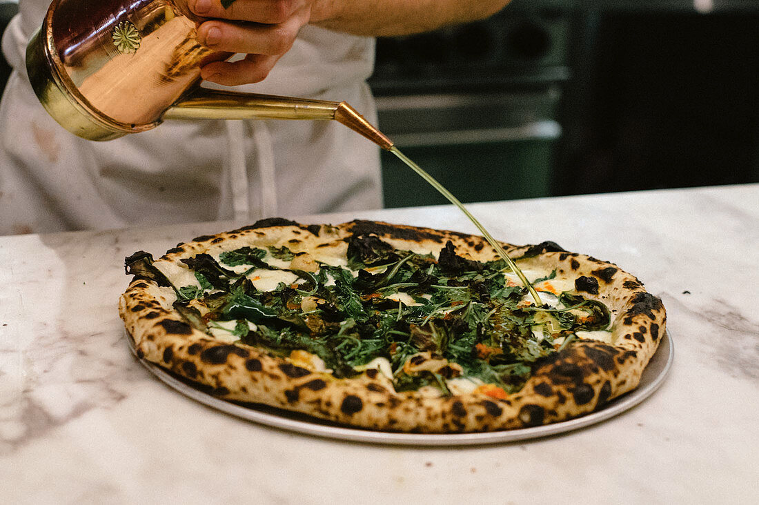Pizza mit Cavolo Nero und Knoblauch wird mit Olivenöl beträufelt