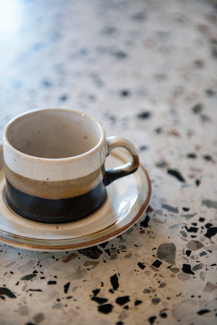 Dreifarbige Steinguttasse und Untertasse auf Terrazzofläche