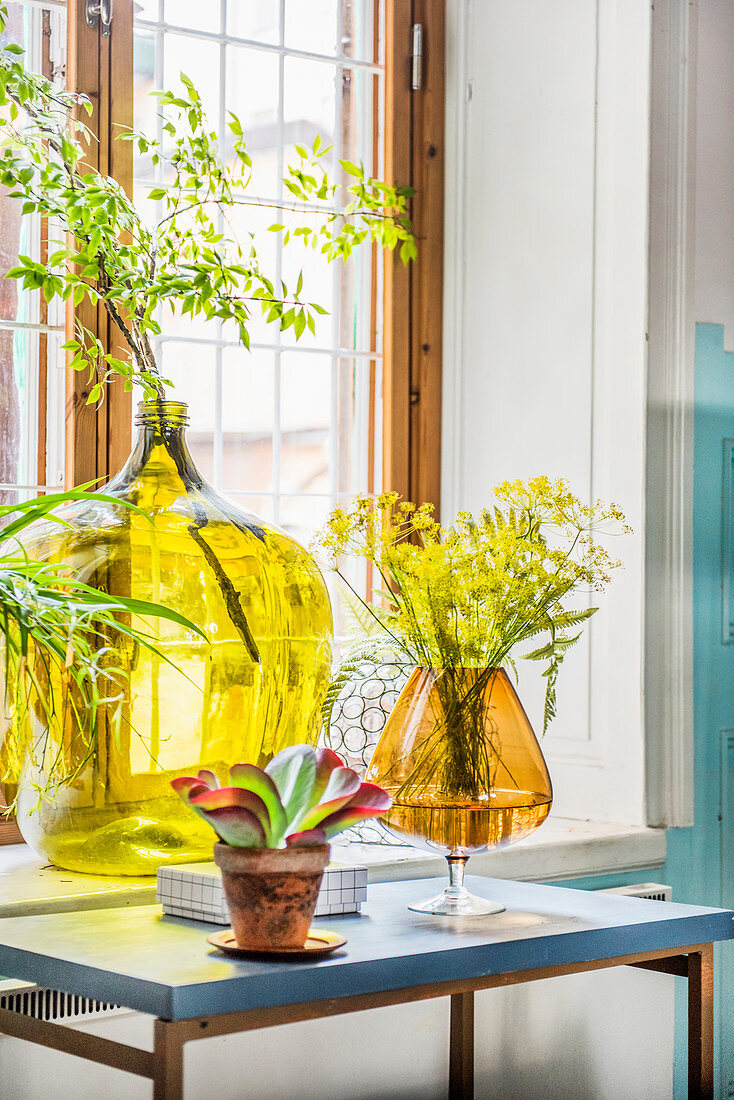 Weinballon und großes buntes Glas als Vasen am Fenster