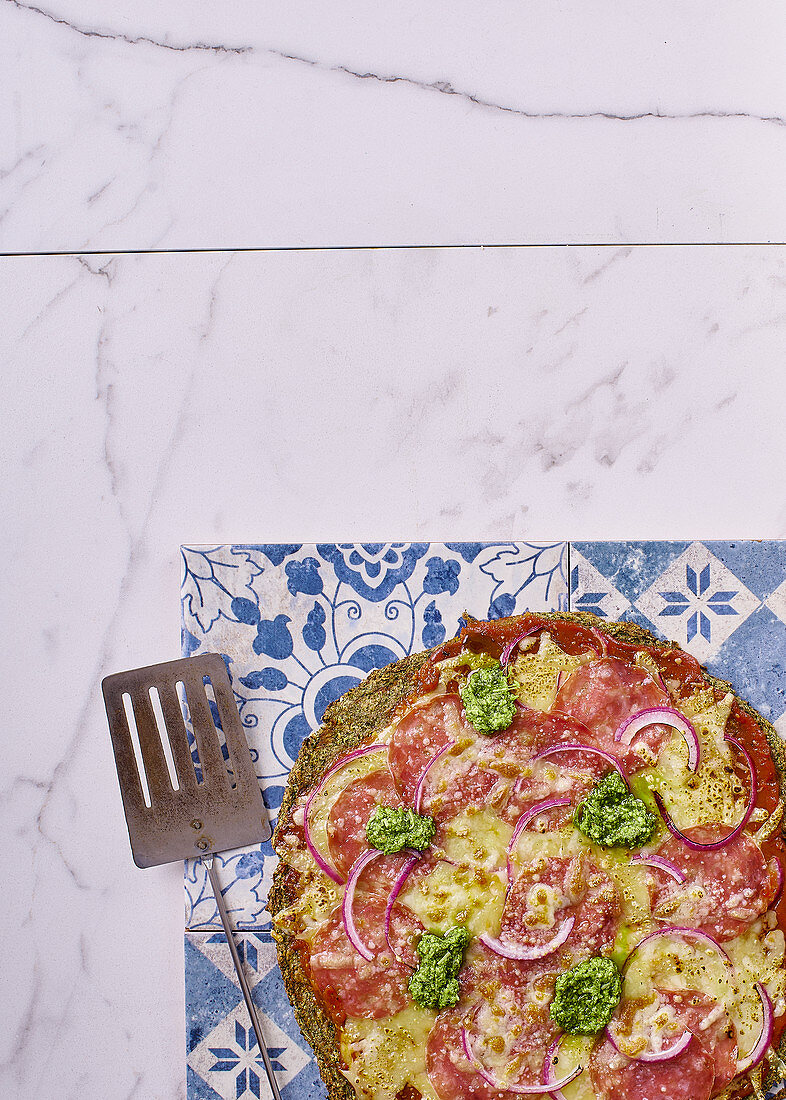 Pizza mit grünem Brokkoli-Spinat-Boden belegt mit Salami und Pesto