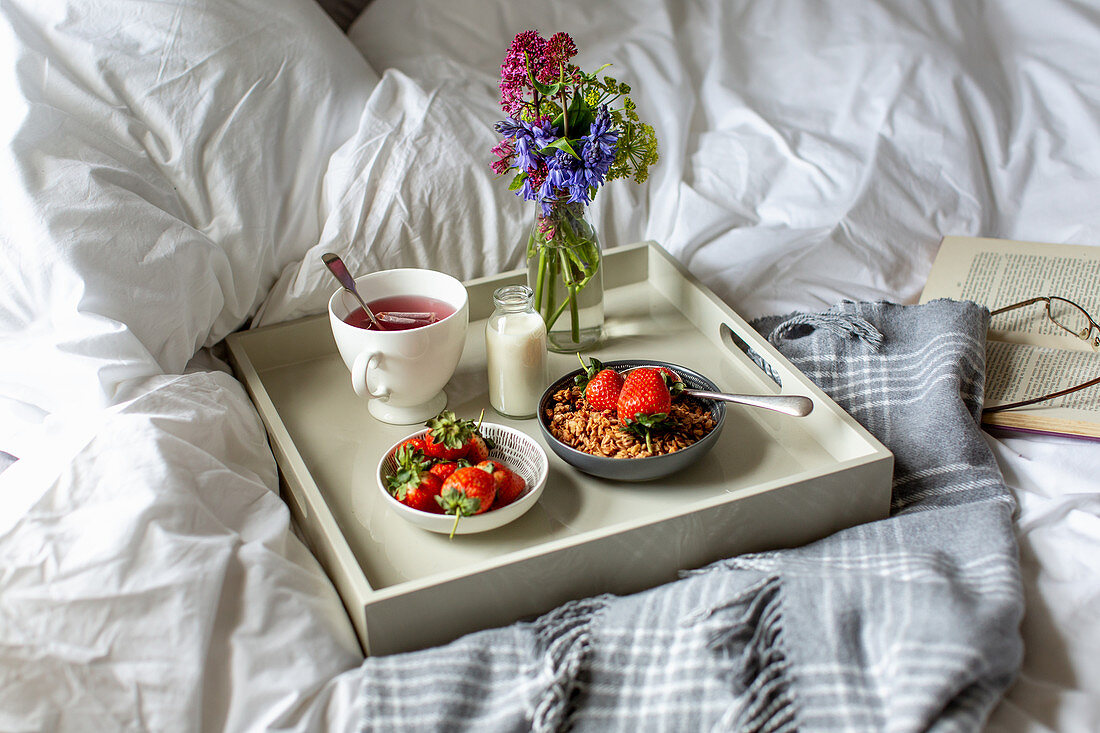 Frühstück im Bett mit Früchtetee, Müsli, Milch und Erdbeeren
