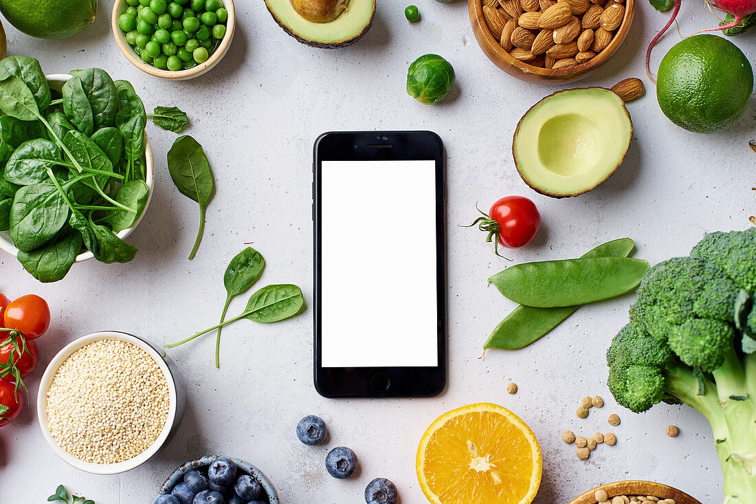 Vegetables, fruit, lentils and almonds arranged around a smartphone