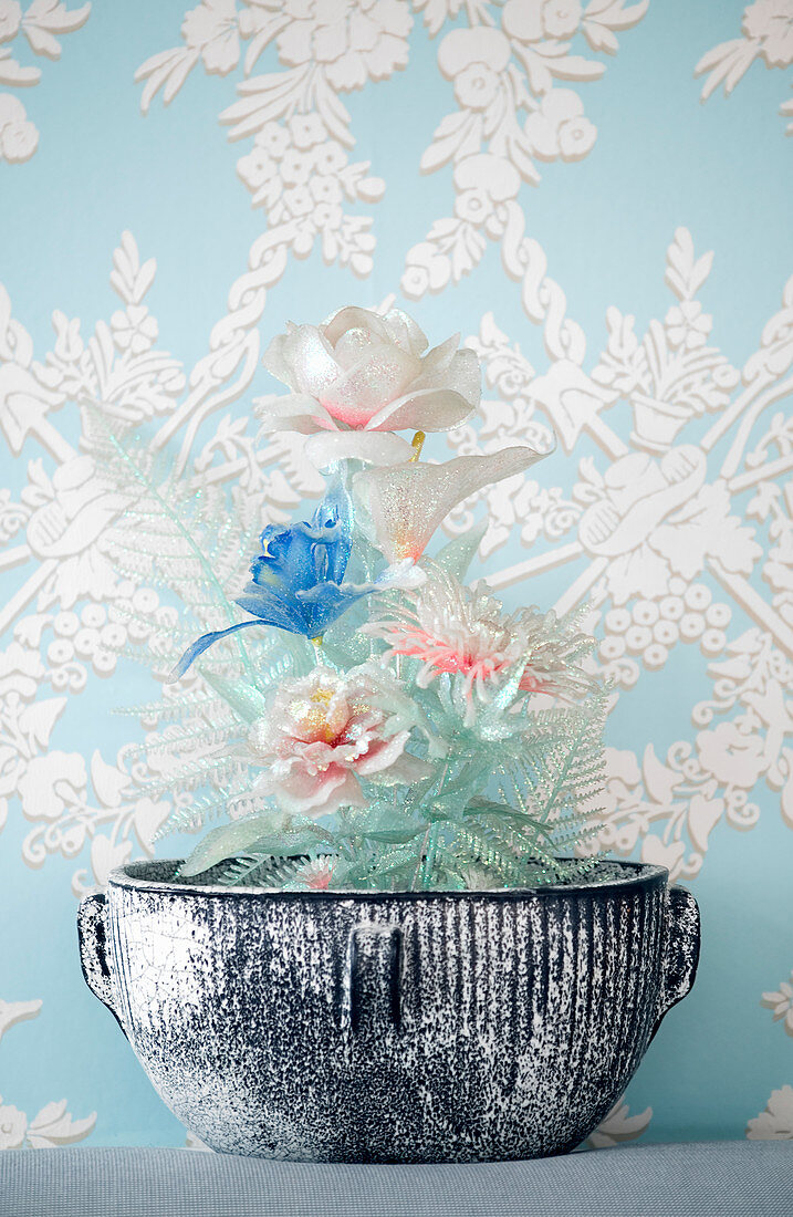 Artificial flowers in bowl against classic patterned wallpaper