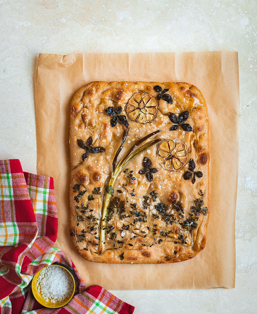 Sourdough focaccia with a flower picture made of herbs, spring onions and garlic