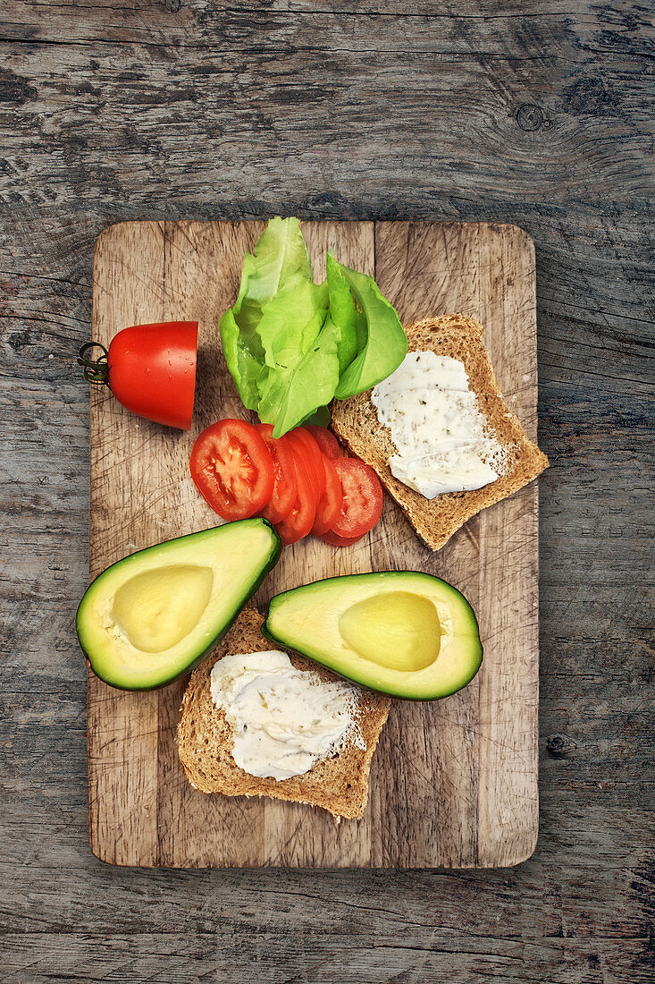 Bread with herb quark, avocado, tomatoes and lettuce on a chopping board