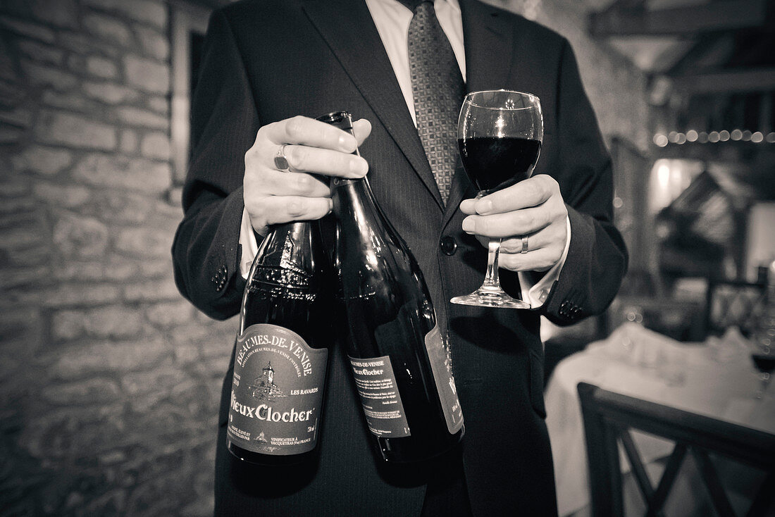 Man holding Wine Glass and Two Bottles of Red Wine at Wedding