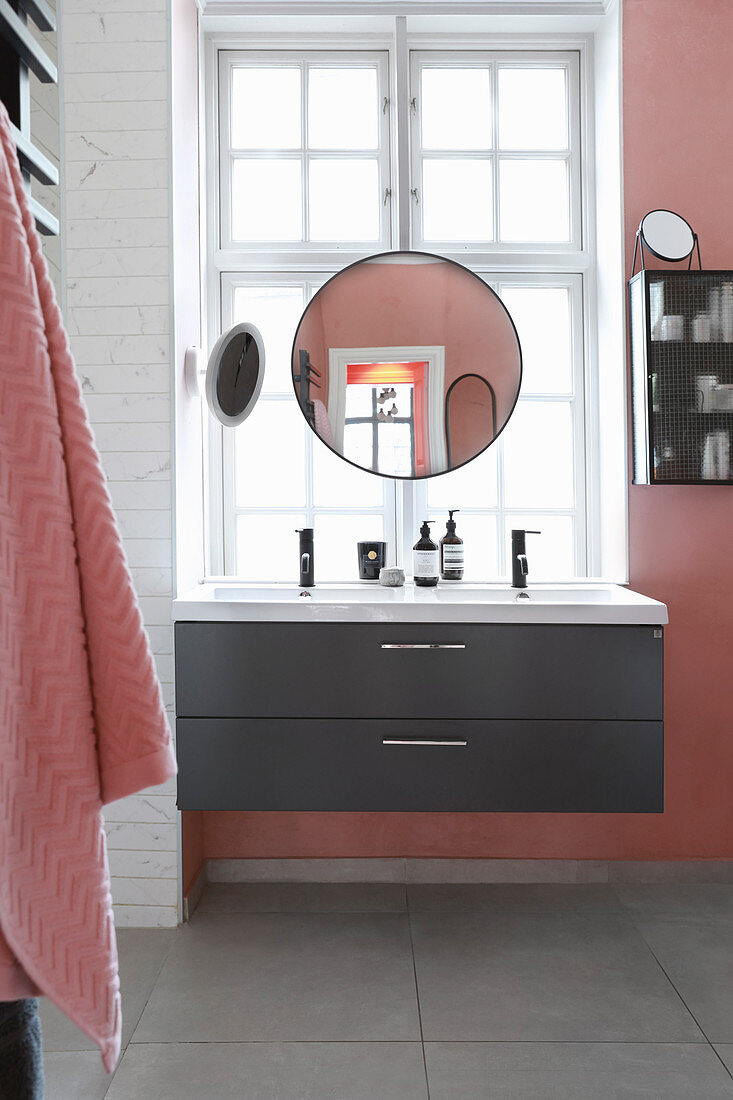 Round mirror above sink and in front of lattice window in pink bathroom