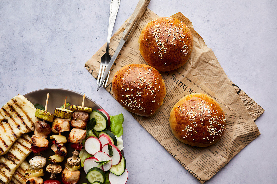 Homemade bread buns served with chicken skewers, grilled halloumi cheese and fresh salad