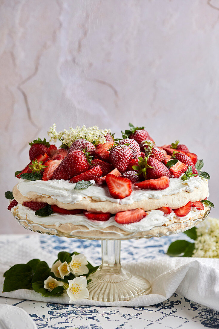 Pavlova cake with fresh strawberries garnished with fresh mint leaves and elderflower