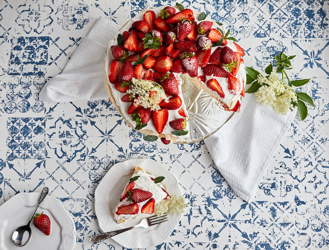 Pavlova cake with fresh strawberries garnished with fresh mint leaves and elderflower