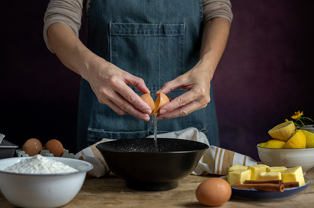 Breaking fresh chicken egg into bowl while cooking pastry in a wooden table with fresh ingredients