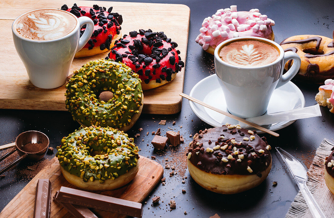 Various doughnuts with sweet toppings and chocolate bars composed with cup of cappuccino on black table