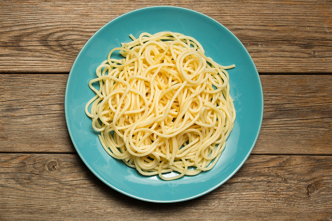 Blue ceramic plate with homemade cooked pasta on dark wooden background