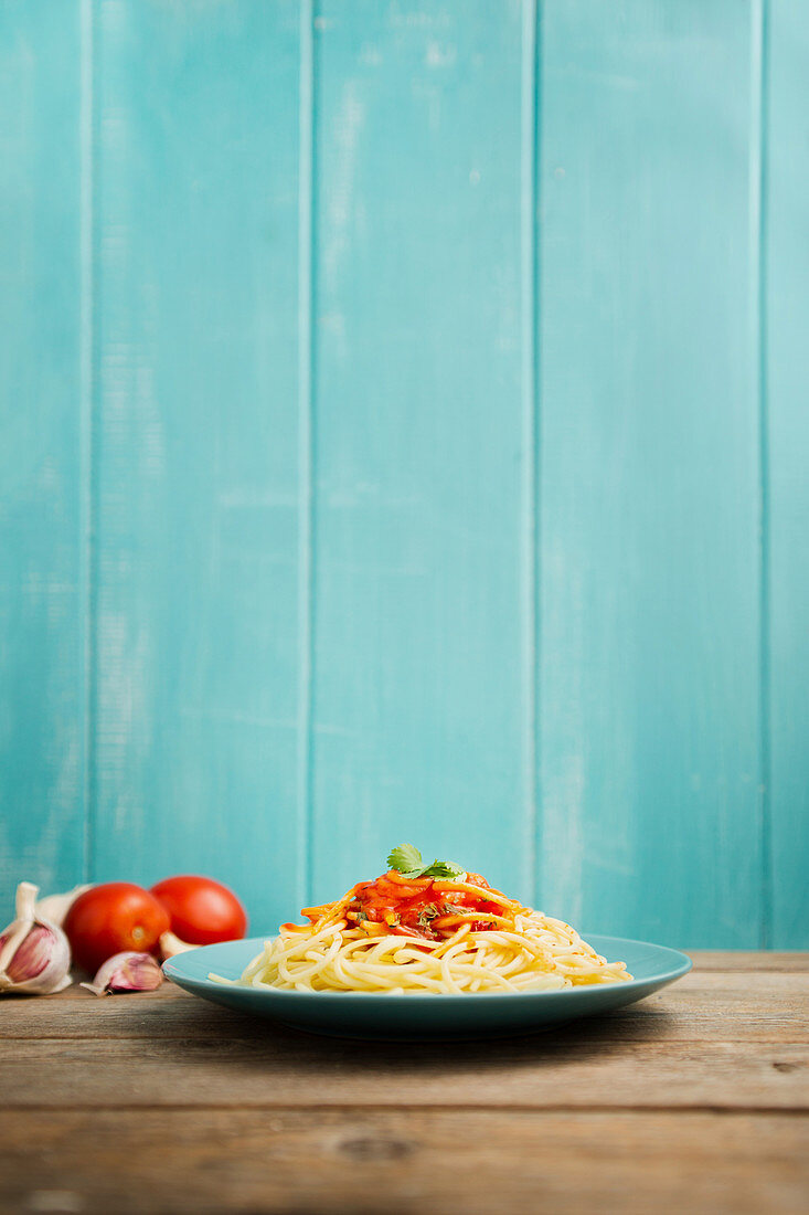 Blue ceramic plate with pasta and tomato sauce decorated with parsley on a wooden table with light blue wooden background