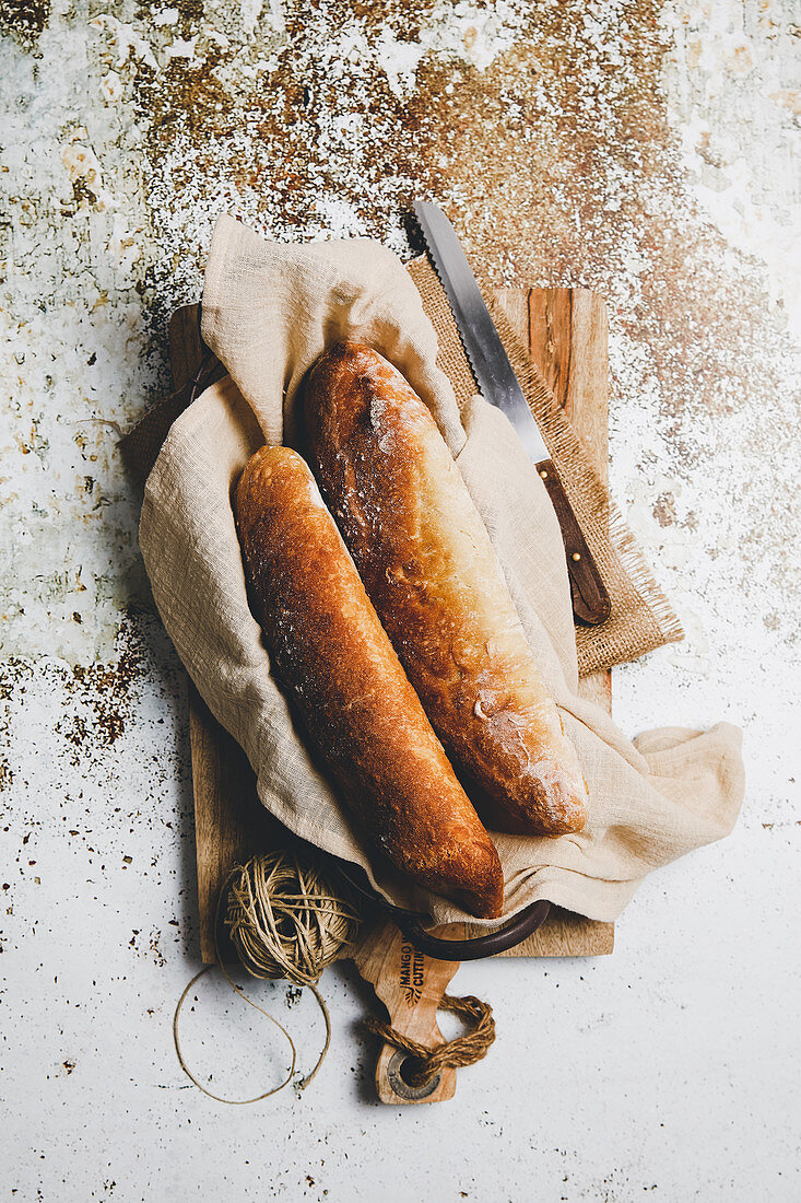 Rustic composition with aromatic bread loaves on board with linen towel and knife on shabby surface