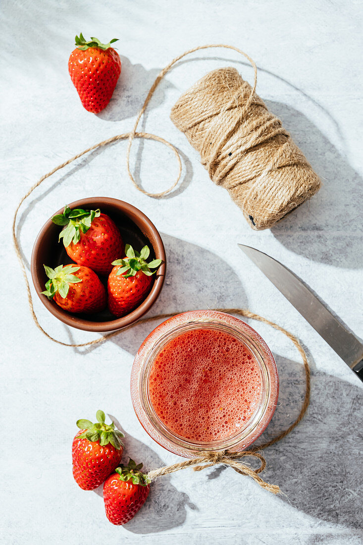 Fresh homemade strawberry juice in glass jar wrapped with twine placed on marble surface