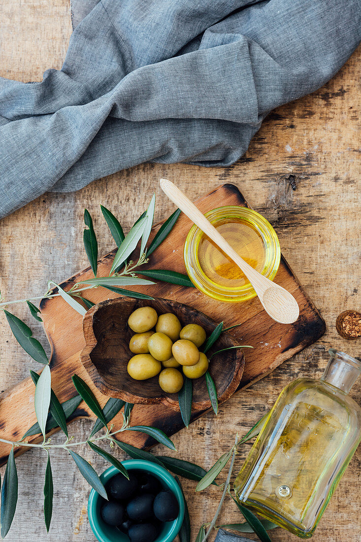 Bio-Olivenöl im Glas zwischen Olivenzweigen und grünen und schwarzen Oliven