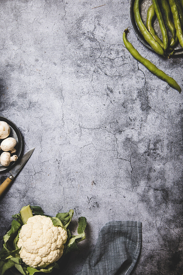 Organic green pods on round metal tray with mushrooms and cauliflower on grunge gray surface