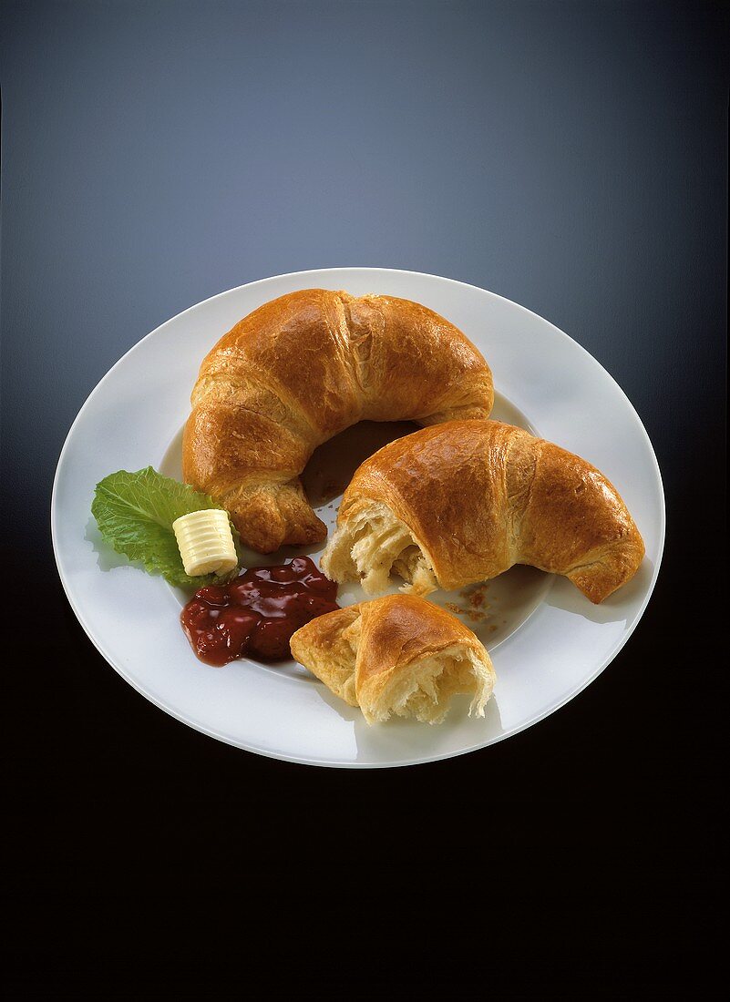 Two croissants on plate with berry jam and butter
