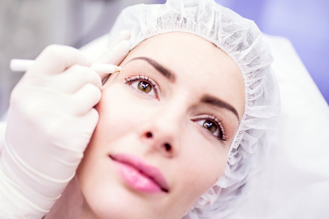 Beauty technician marking woman's face for treatment