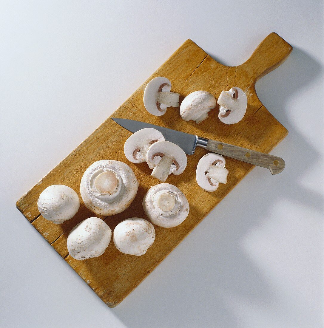 Button Mushrooms on a Cutting Board with a Knife; Some Sliced