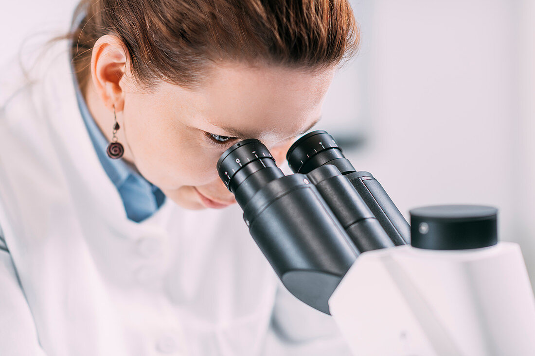 Young female archaeologist with microscope