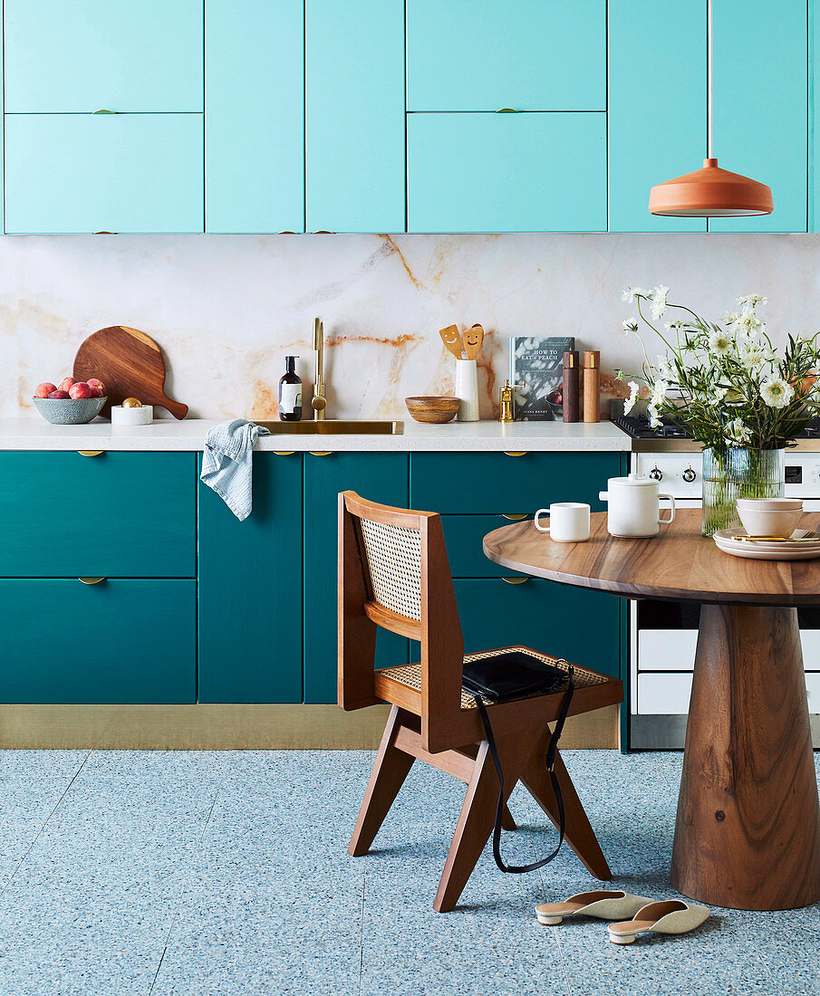 Küchenzeile in Blautönen, Tapete in Marmoroptik, runder Holztisch und Designerstuhl,
