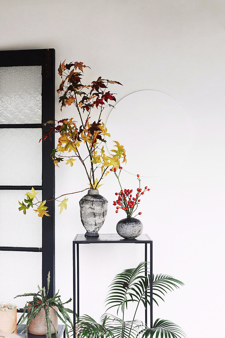 Zweige mit Herbstlaub und Hagebutten in Vasen