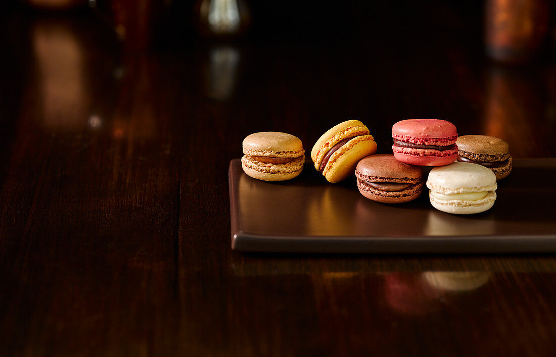 Verschiedene Macarons auf Servierplatte vor dunklem Hintergrund