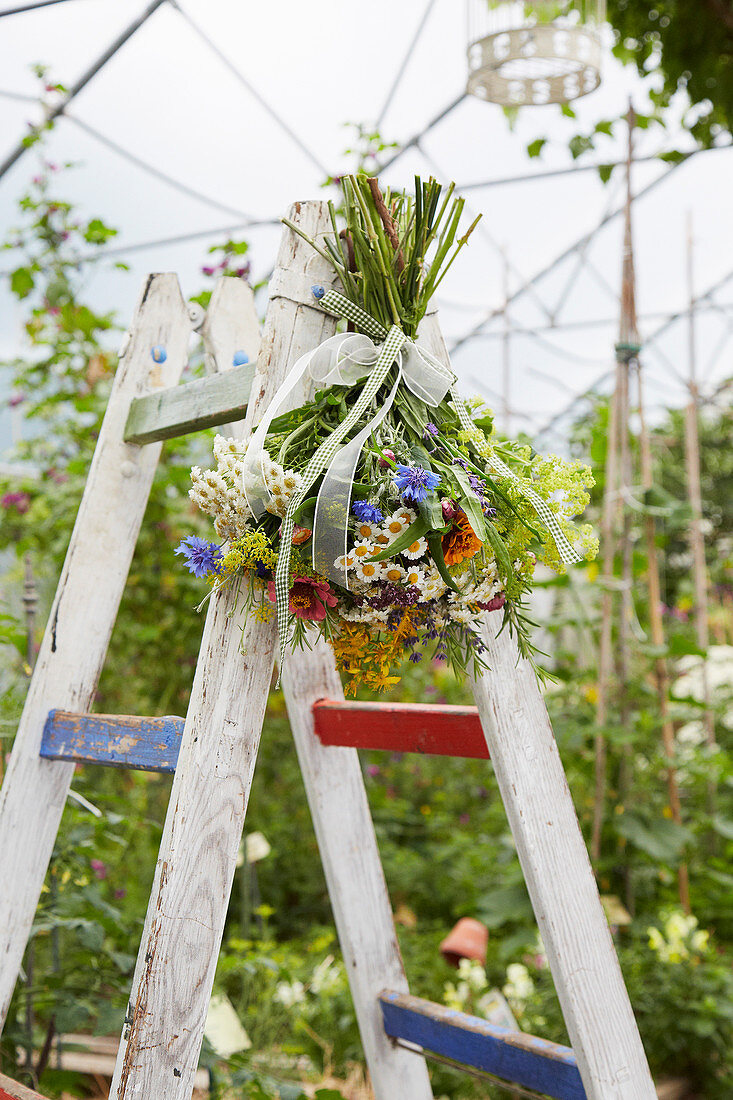 Sommerlicher Blumenstrauß hängt an einer Leiter im Gewächshaus