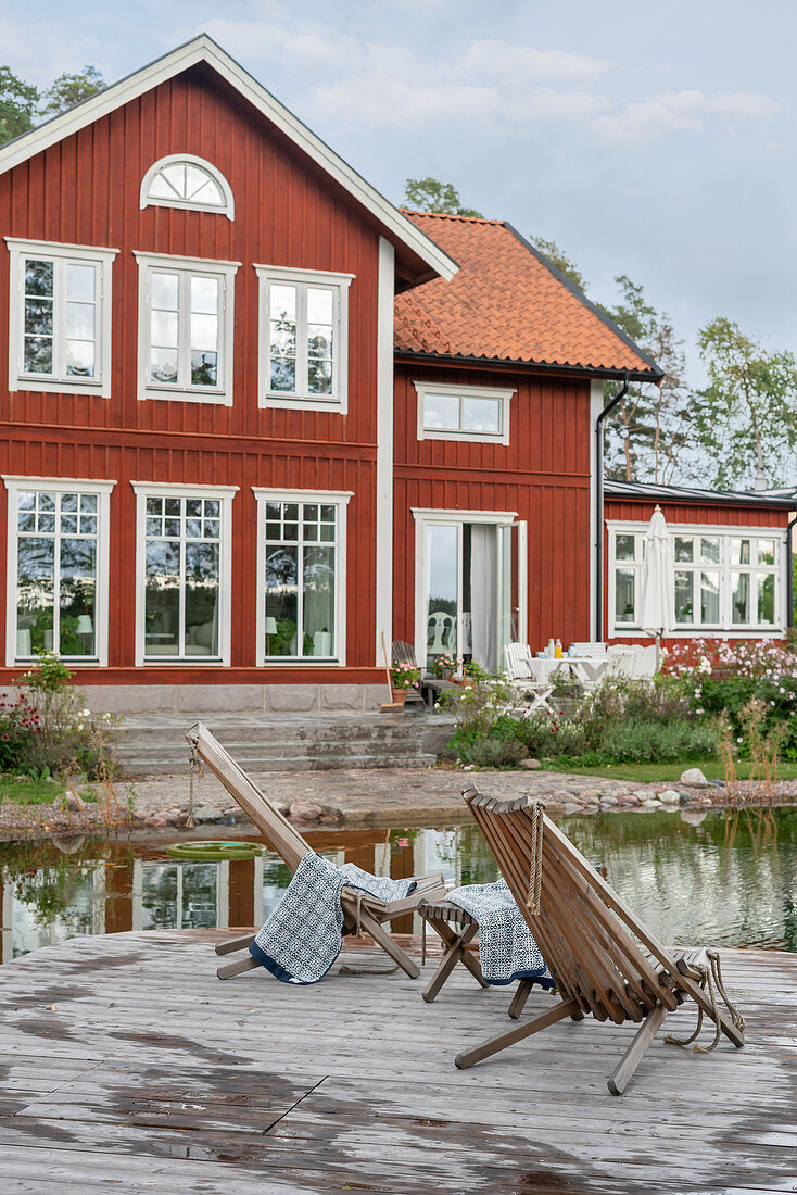 Loungers on jetty next to pond outside Falu-red Swedish house