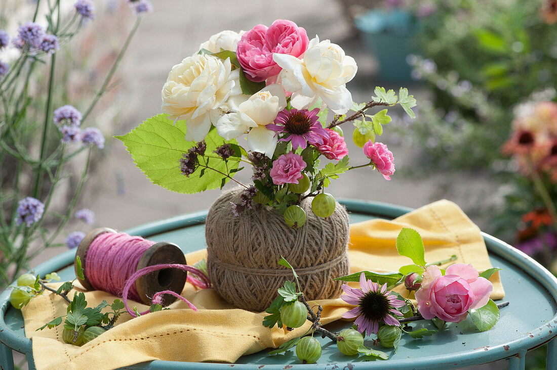 A small bouquet of roses, a sun hat, oregano and gooseberry in a spool of thread