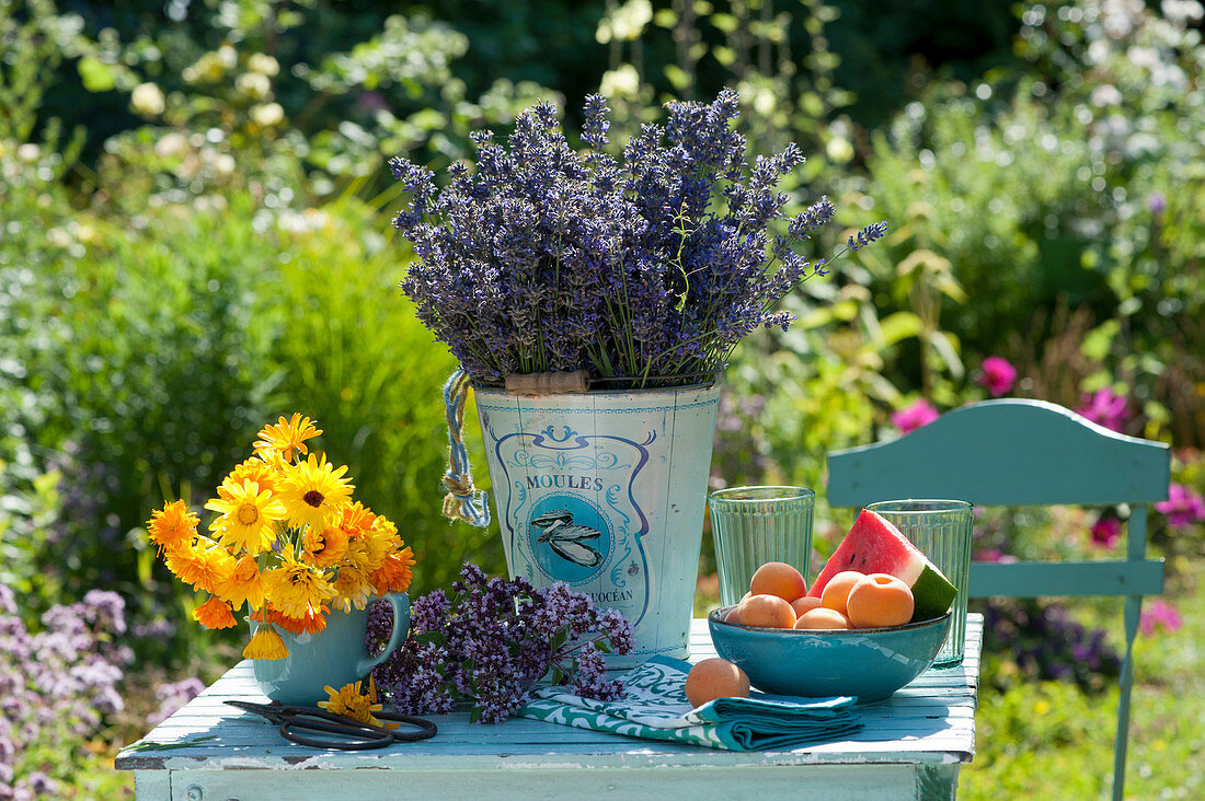 Lavendel - Strauß, Ringelblumen, Oreganoblüten und Schale mit Aprikosen und Wassermelone auf Tisch im Garten